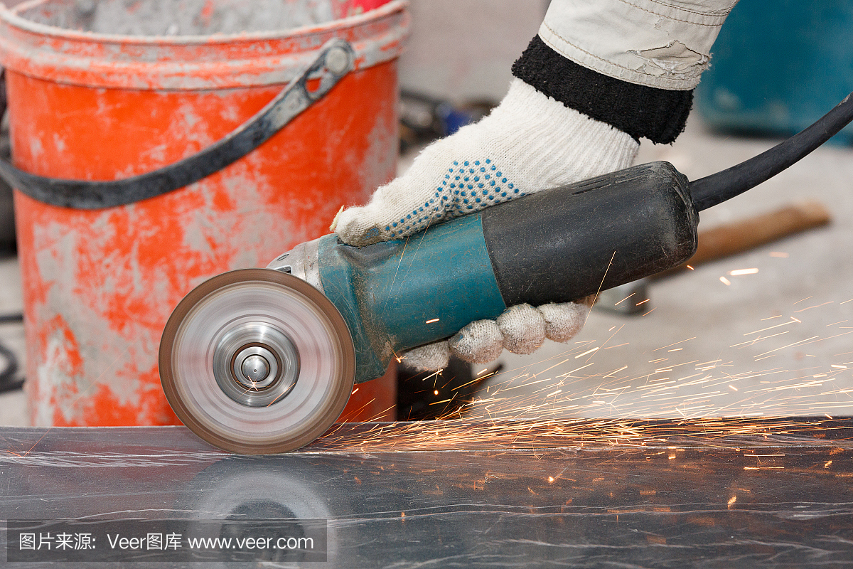 戴手套的工人的手用有棱角的研磨机切割建筑材料,产生火花。